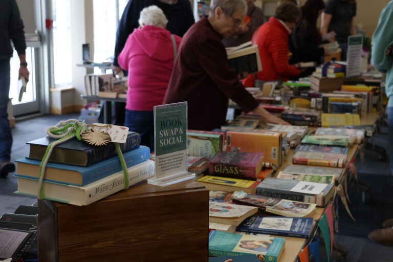 Book Swap & Social, view of the table with books laid out and guests browsing some of the books